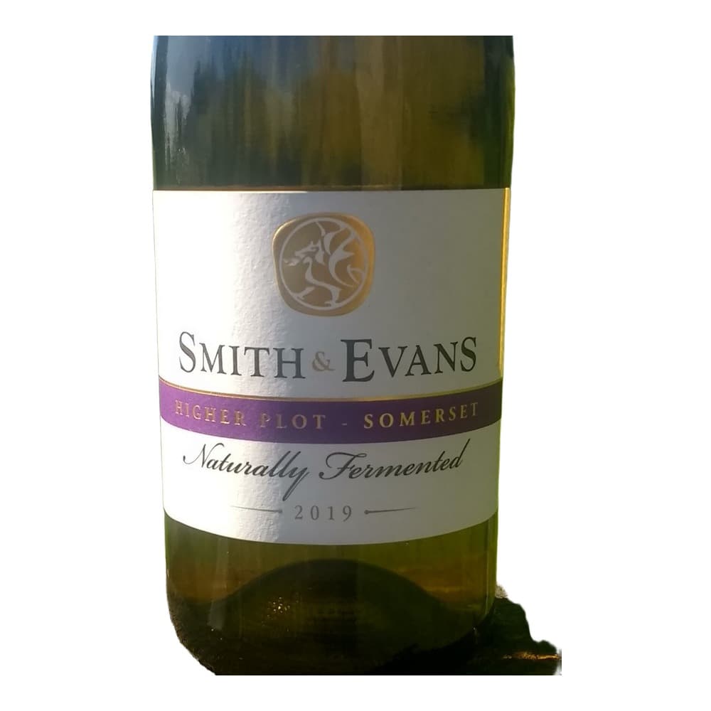 A bottle of Smith & Evans Higher Pinot Somerset 2019 naturally fermented wine displayed outdoors with rolling green vineyards in the background.