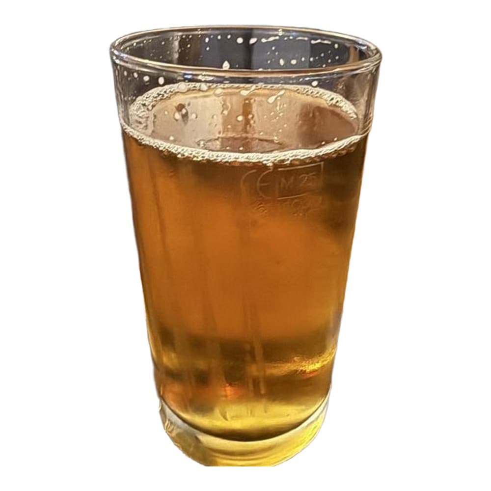 A glass of pale golden beer with a foamy head sits on a wooden table in a pub or bar setting, with coasters and a blurred background.