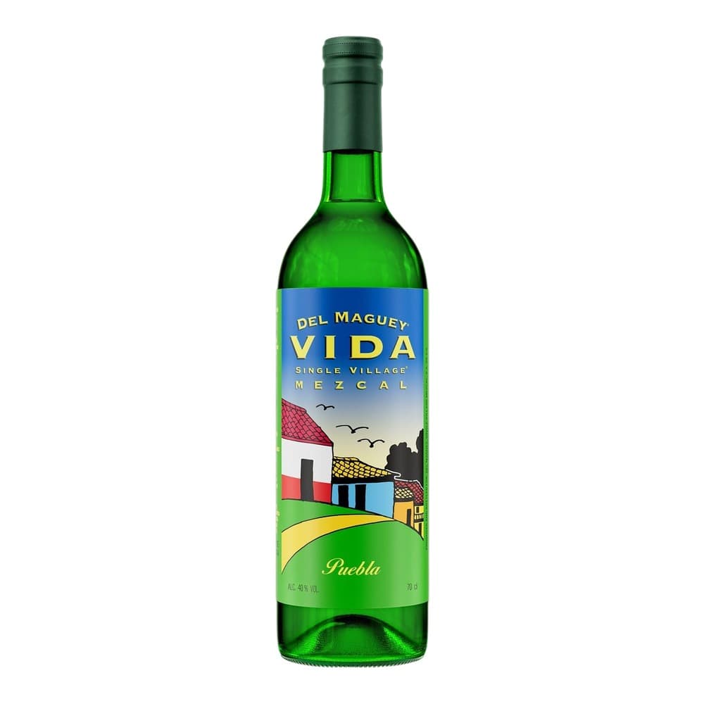 A green glass bottle of Del Maguey Vida mezcal with a blue and colourful village-themed label featuring a white and red building, against a plain white background.