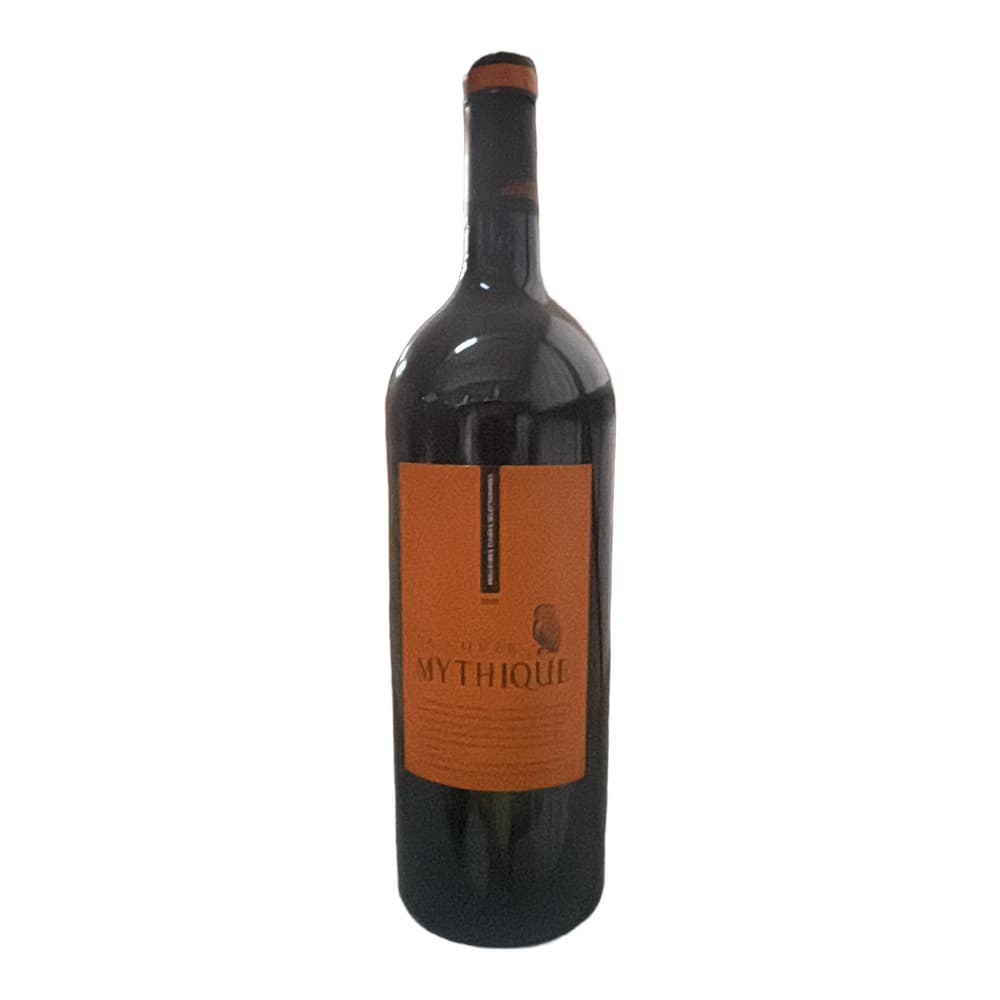 A bottle of Mythique red wine with an orange label displayed on a white shelf against a warehouse background.
