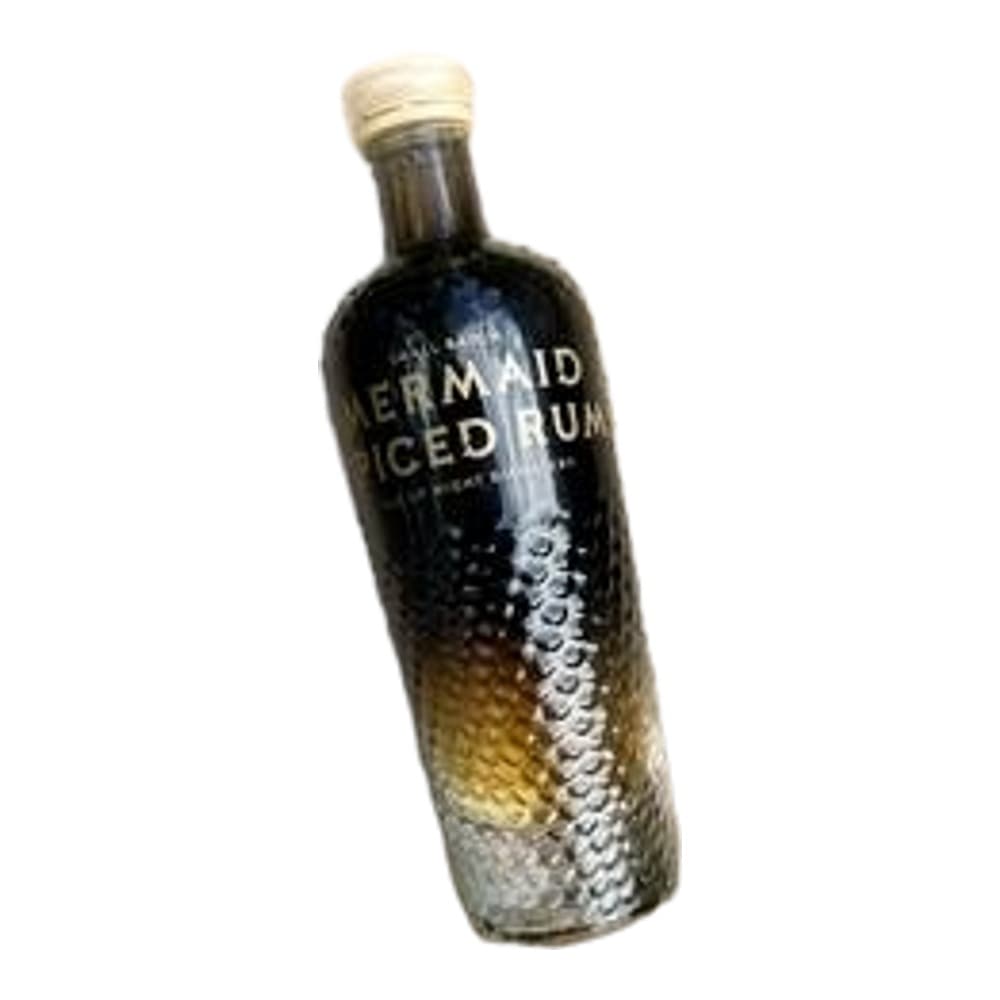 A black glass vodka bottle with gold cap and decorative labelling, positioned on a white and beige textured surface with scattered sand-like material.