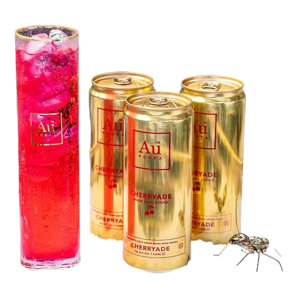 A pink cocktail drink in a tall glass next to three golden cans of Ati Cherryade vodka, styled outdoors with decorative elements and ice.