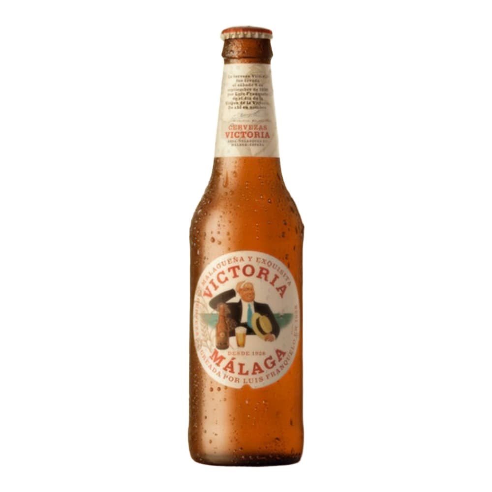 A chilled bottle of Victoria Málaga beer with a brown label featuring a man illustration, positioned on a wooden surface against a beige textured wall with dramatic shadows.