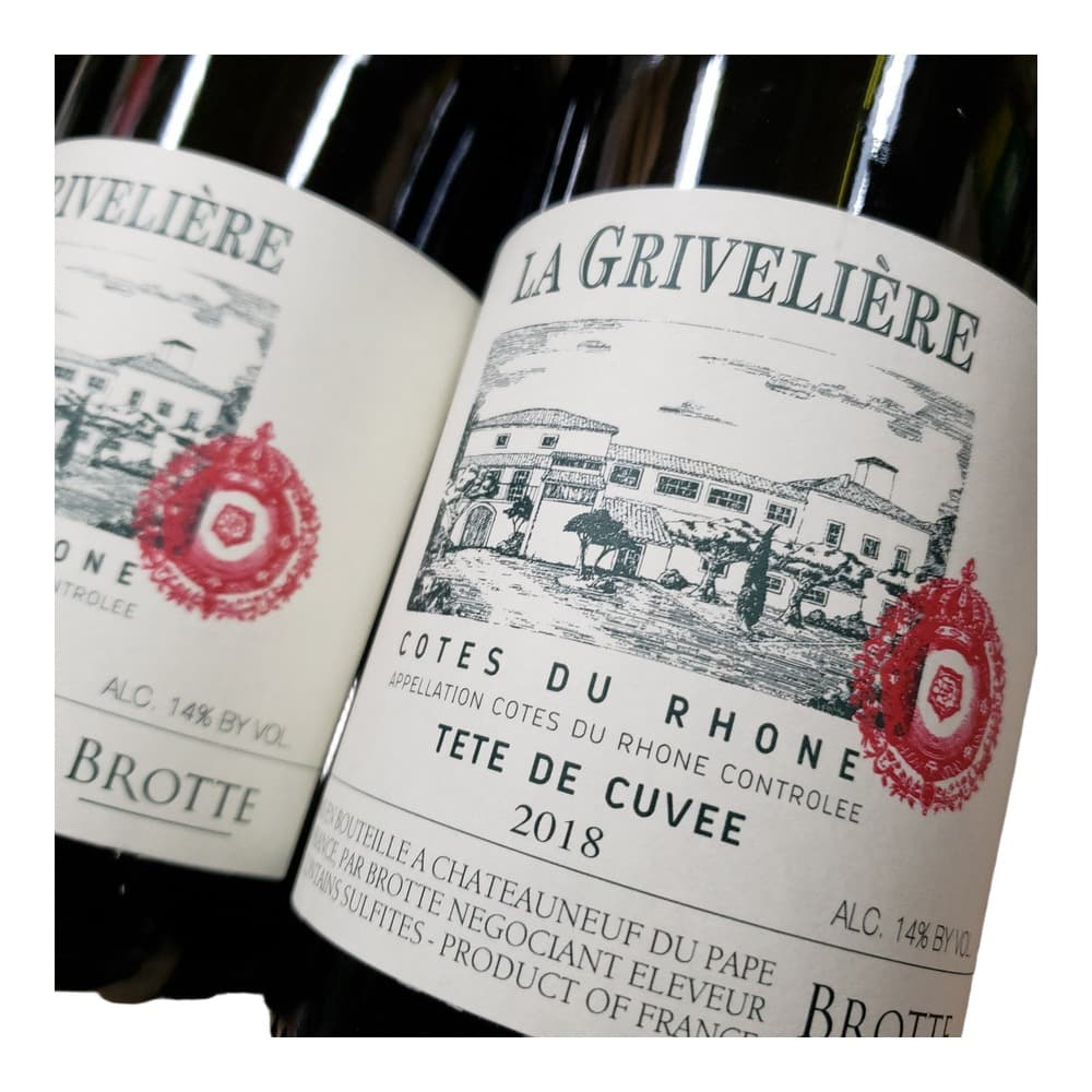 Two wine bottles with cream-coloured labels featuring architectural illustrations and red wax seals, displayed against a dark background with additional wine bottles blurred in the background.