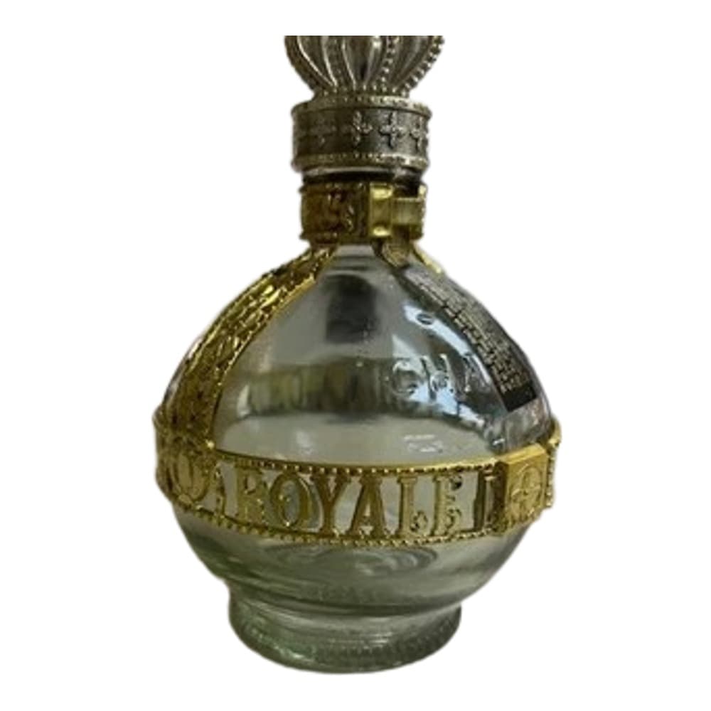 A decorative perfume bottle with a brass crown-shaped stopper and ornamental brass band around clear glass, displayed on a neutral surface
