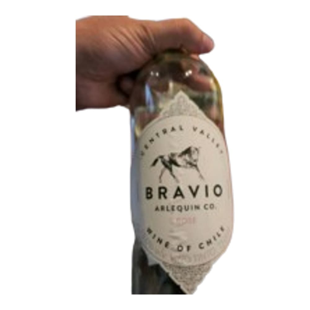 A person's hand holding a bottle of Bravio wine with a white label against a blurred indoor background