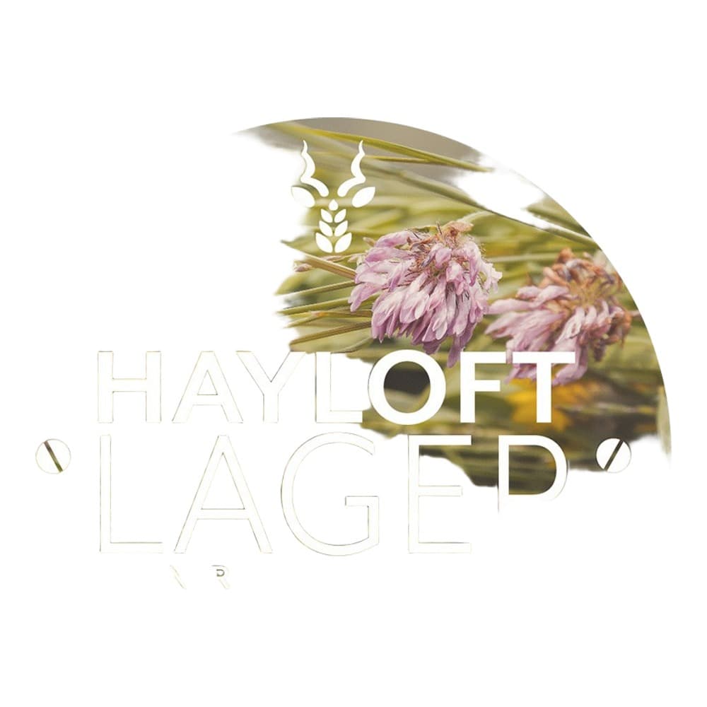Circular beer label for Hayloft Lager Pilsner by Three Acre Brewery, featuring purple flowers and green wheat imagery with white text on a botanical background.