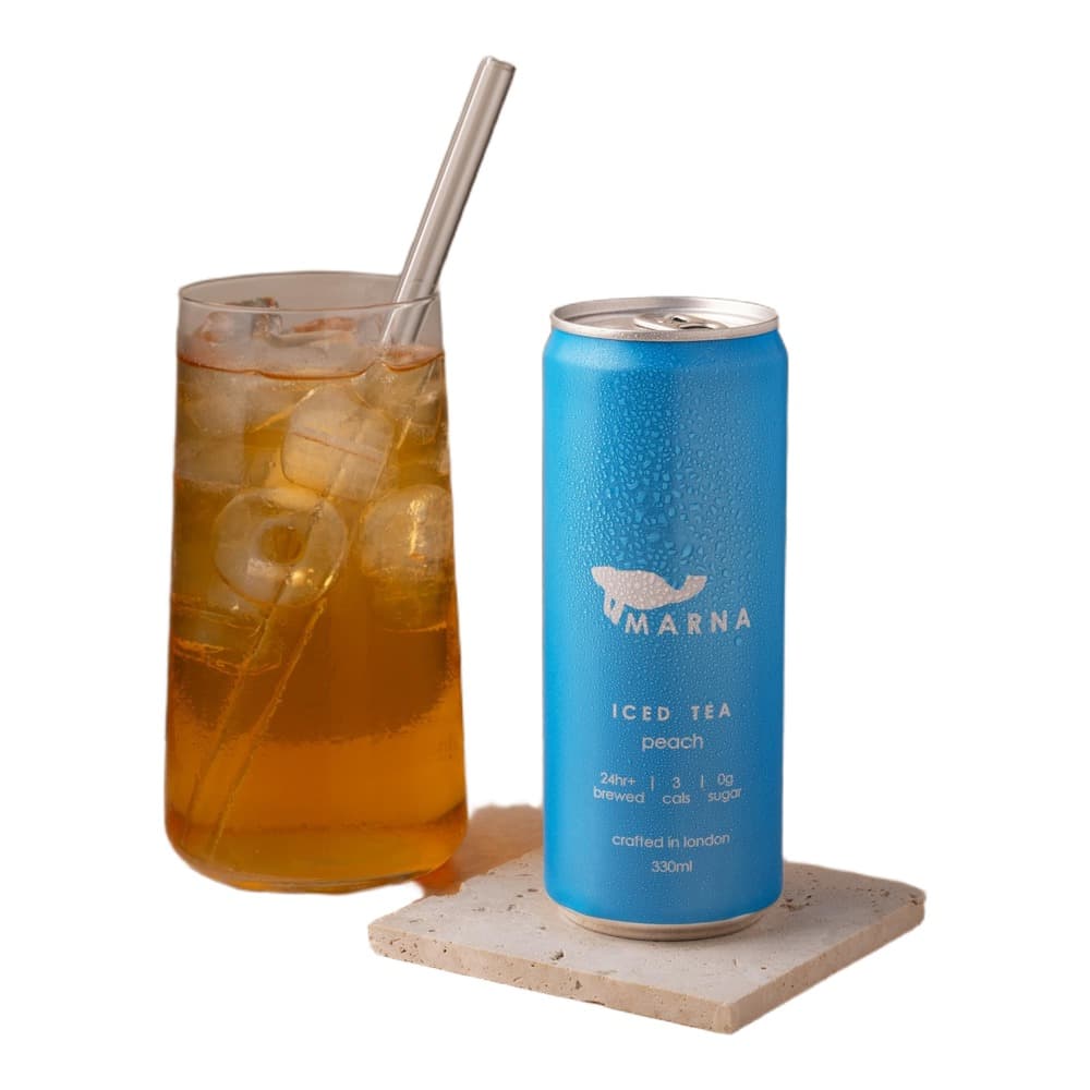 Blue Umarna iced tea peach can next to a glass of iced tea with straw on a neutral background