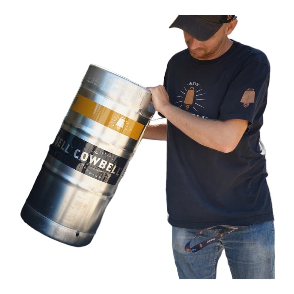 A man in a black t-shirt and cap loading a large metal Bill Cowbel beer keg into the open boot of a car on a sunny day.