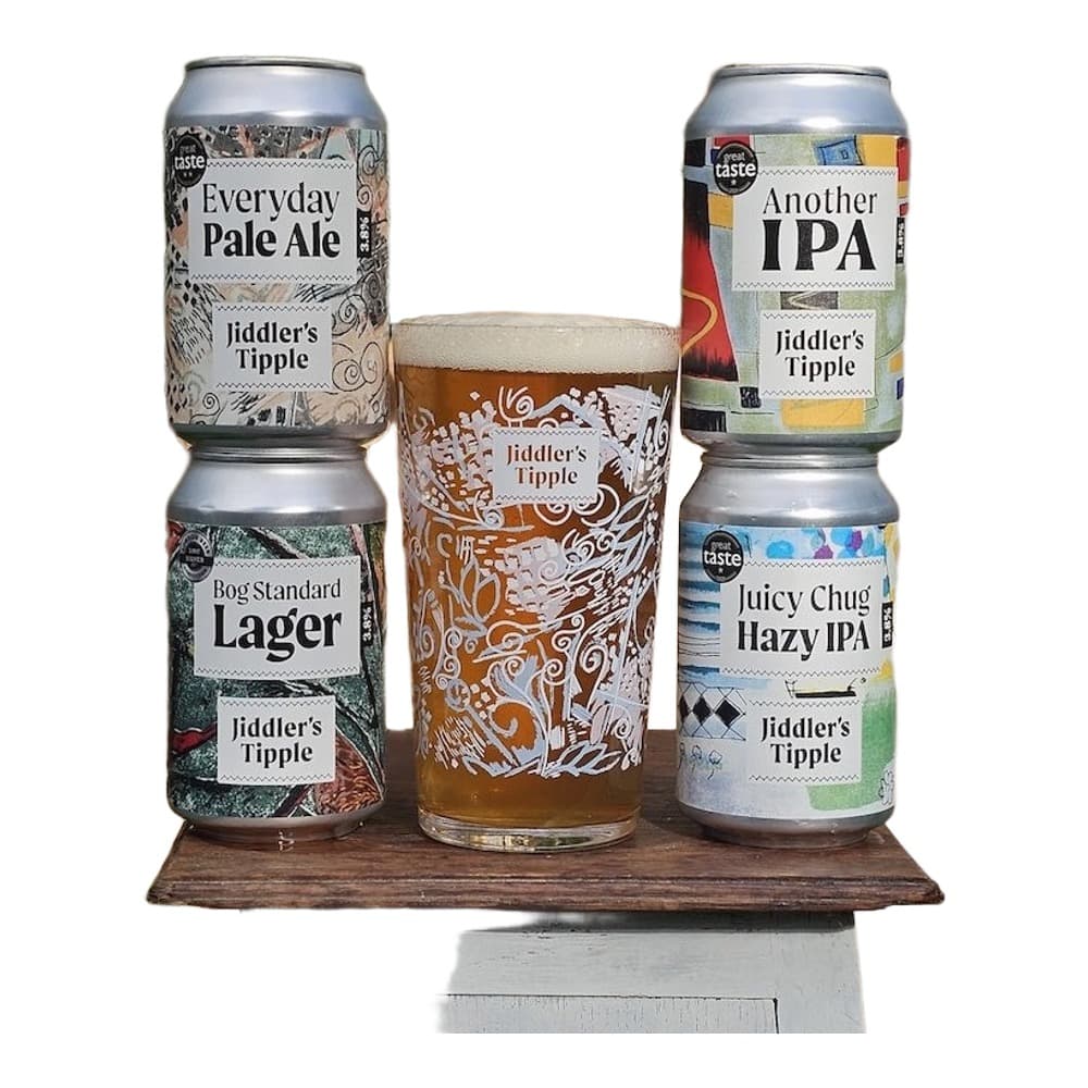 Four Jiddler's Tipple branded beers displayed on a wooden platform outdoors, including cans and a pint glass with beer.