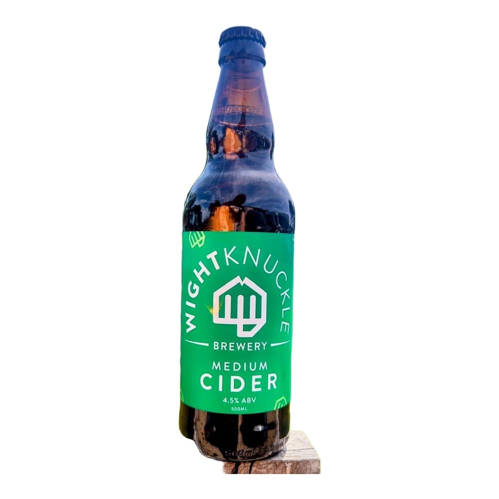 A bottle of Wightknuckle Brewery Medium Cider displayed on a wooden block in a lush green garden landscape with trees and wildflowers in the background.