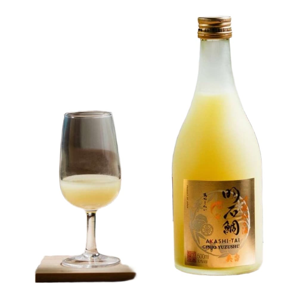 A bottle of Akashi-Tai Ginjo Yuzu sake next to a glass of pale yellow liquid, accompanied by fresh lemons in a blue bowl on a light wooden table