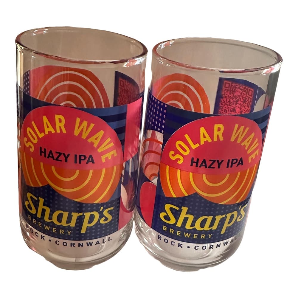 Two clear glass beer glasses featuring Solar Flare Hazy IPA branding from Sharp's Brewery in Rock, Cornwall, displayed against a white background.