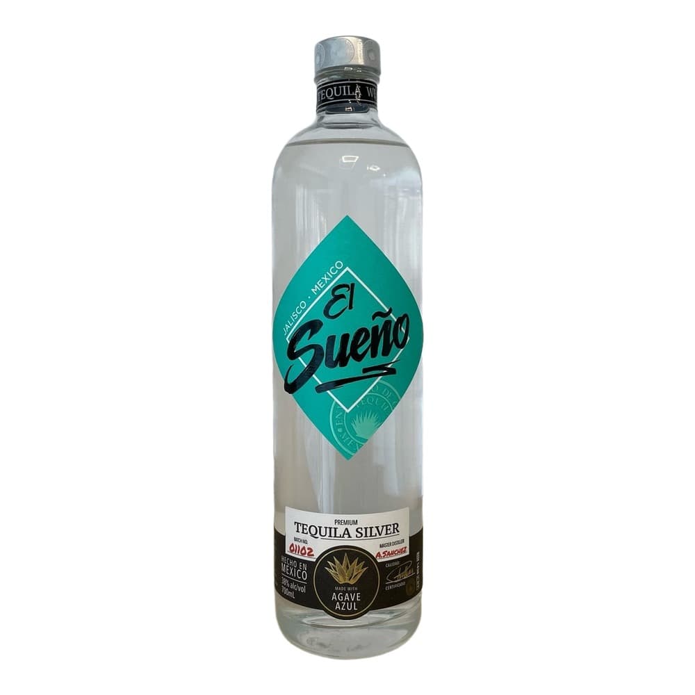 A clear glass bottle of El Sueño Tequila Silver with a turquoise diamond-shaped label featuring the brand name, displayed against a plain light grey background on a wooden surface.