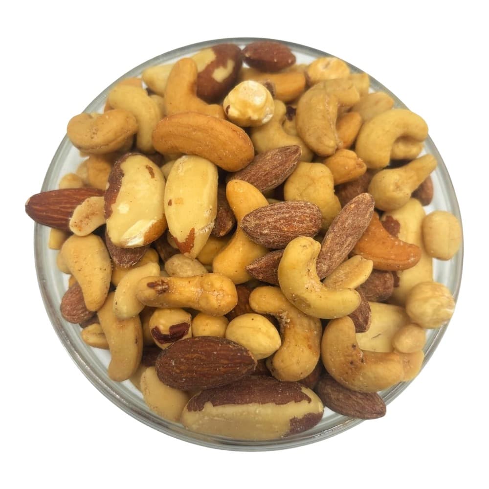 Assorted roasted nuts including almonds, cashews, and macadamia nuts served in a round glass bowl on a white background